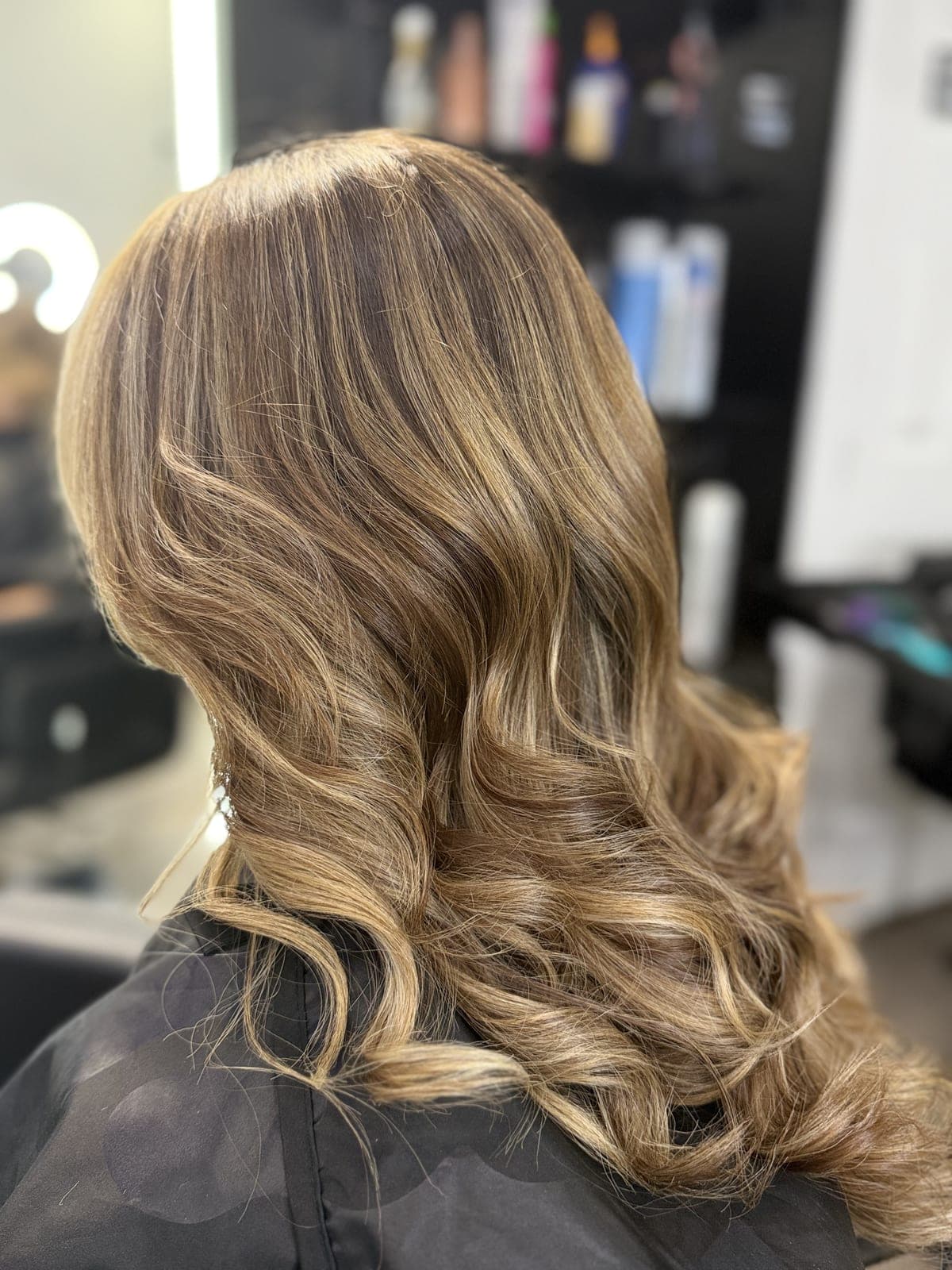 Bronde balayage on shoulder-length hair styled in soft waves, salon mirror in the background