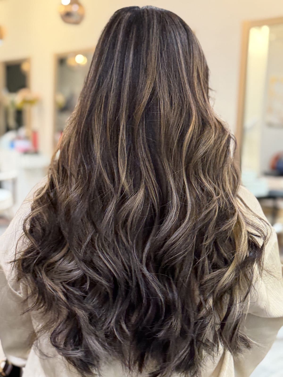 Long dark brown hair with hand-painted caramel balayage, styled in loose waves, seen from the back