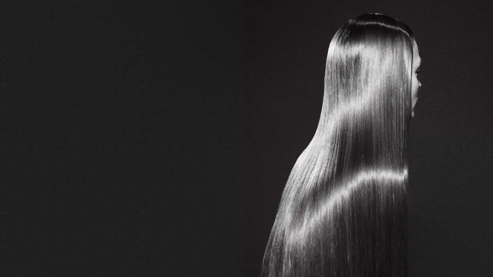 Long, poker-straight hair with a mirror-smooth finish, seen from behind against a dark studio background