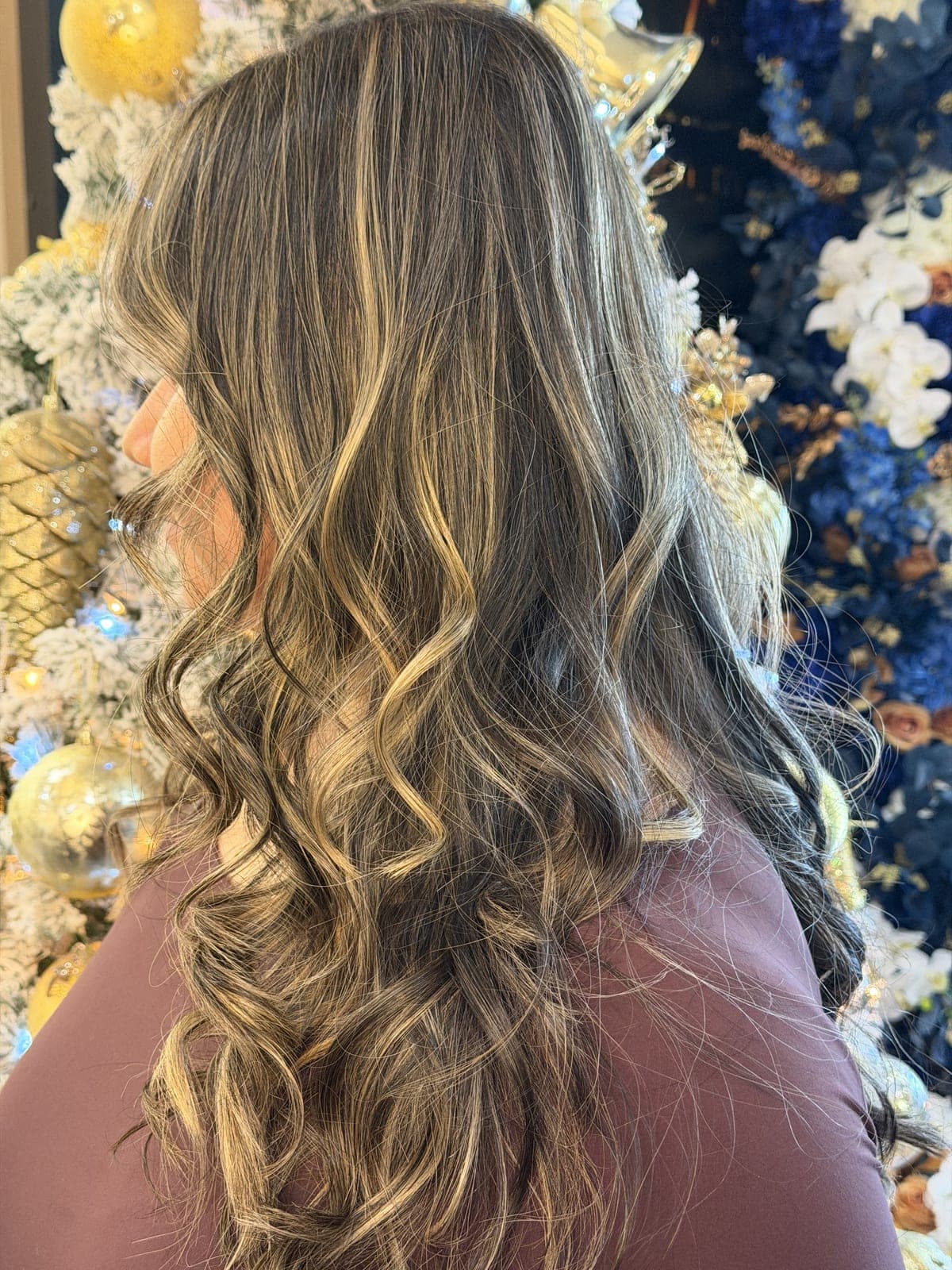 Long dark hair with bright blonde highlights concentrated around the face, holiday decorations behind