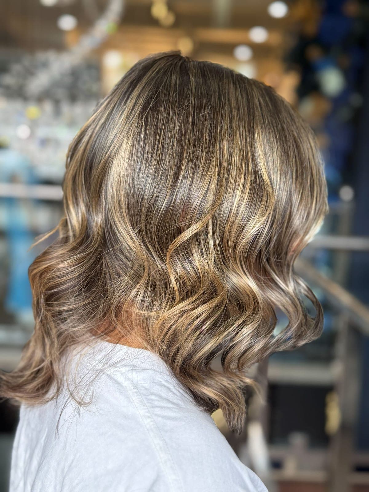 Hand-painted blonde balayage on mid-length hair, styled in soft waves, seen from the side in the salon