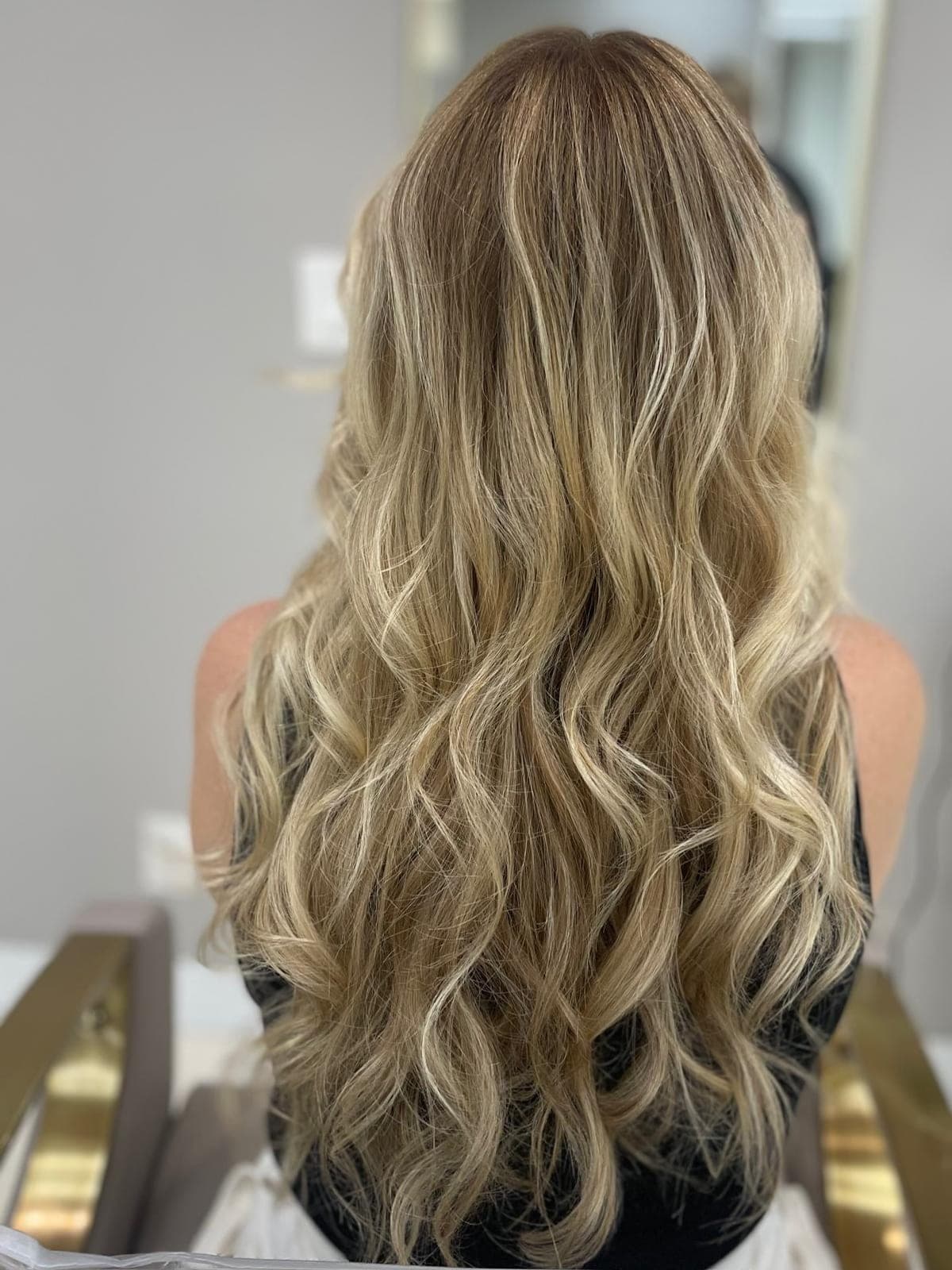 Fine highlights through long bronde hair styled in soft waves, seen from the back