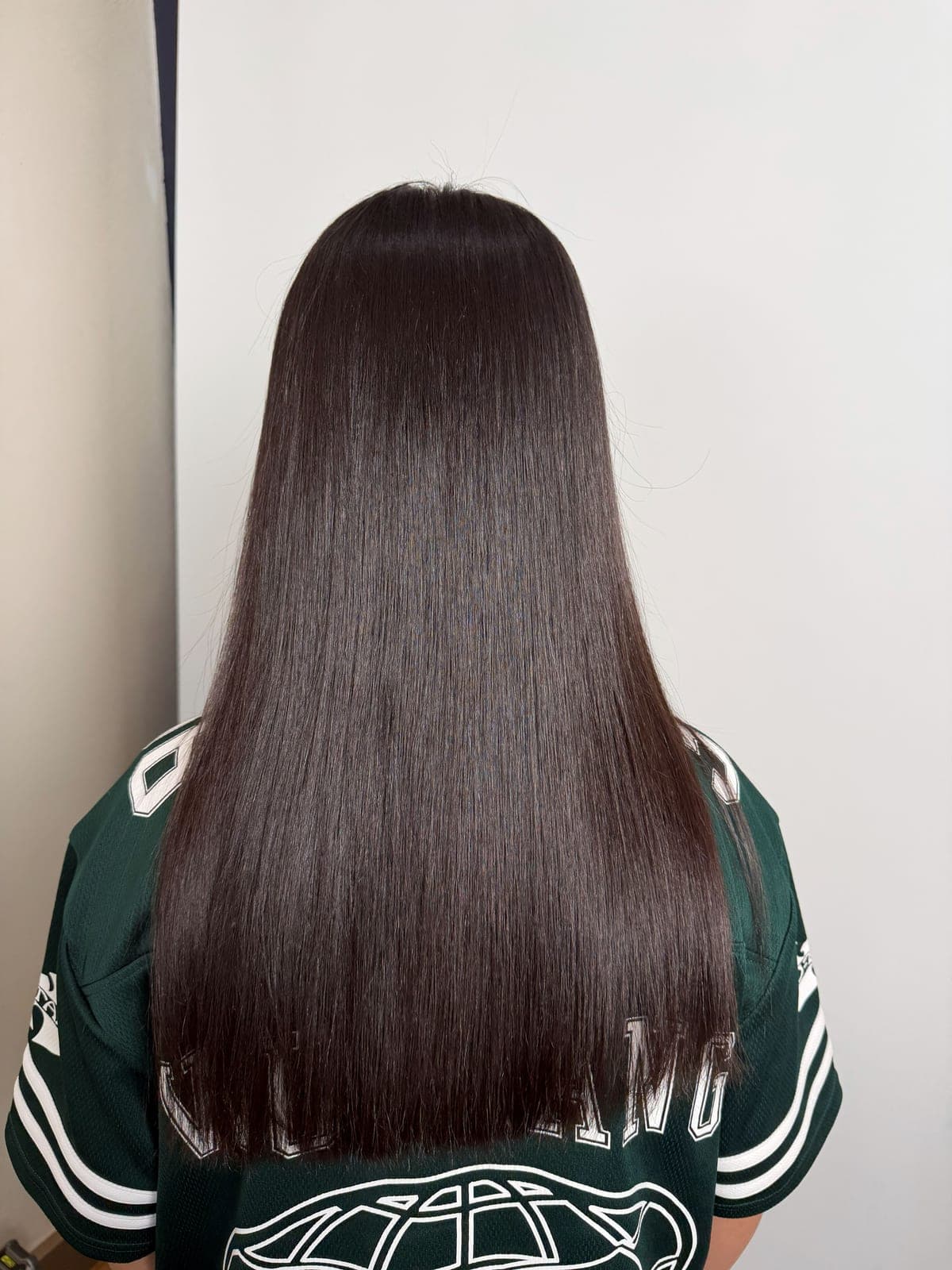 Dark brown hair after a smoothing treatment, falling glass-straight and glossy, seen from the back
