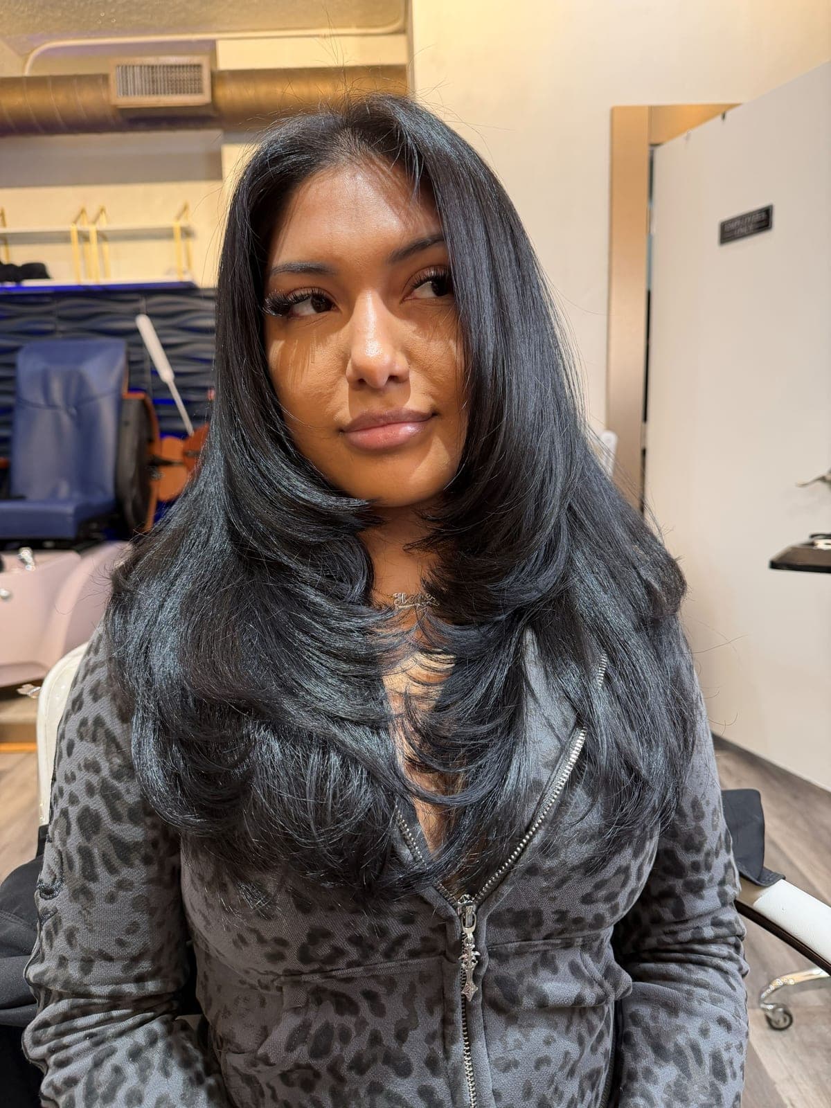 Long dark hair cut into face-framing layers, client facing the camera in the salon
